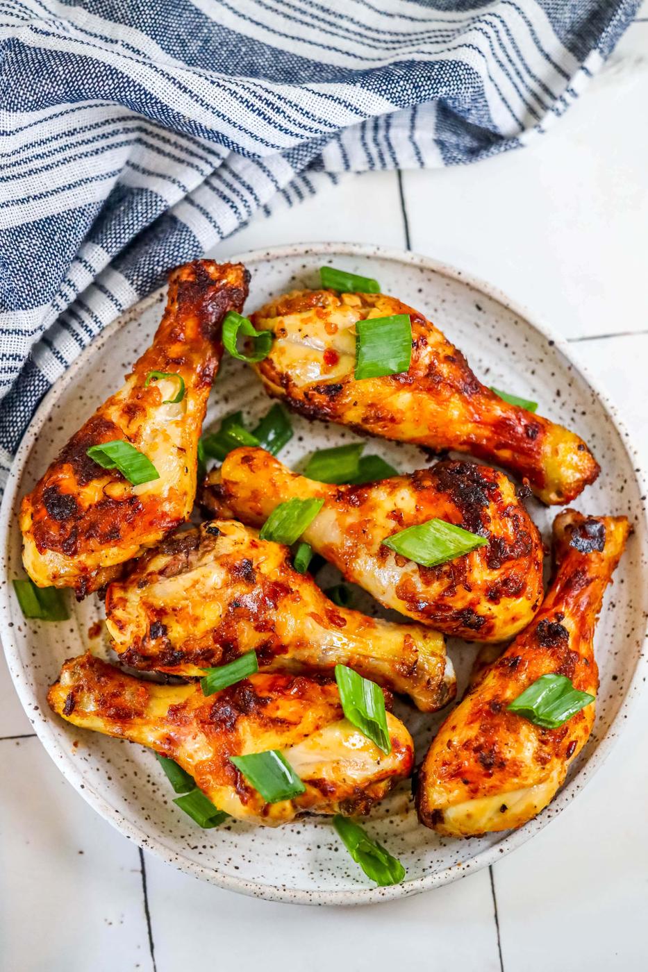 picture of spiced chicken drumsticks with green onions on it on a white plate with a blue towel.
