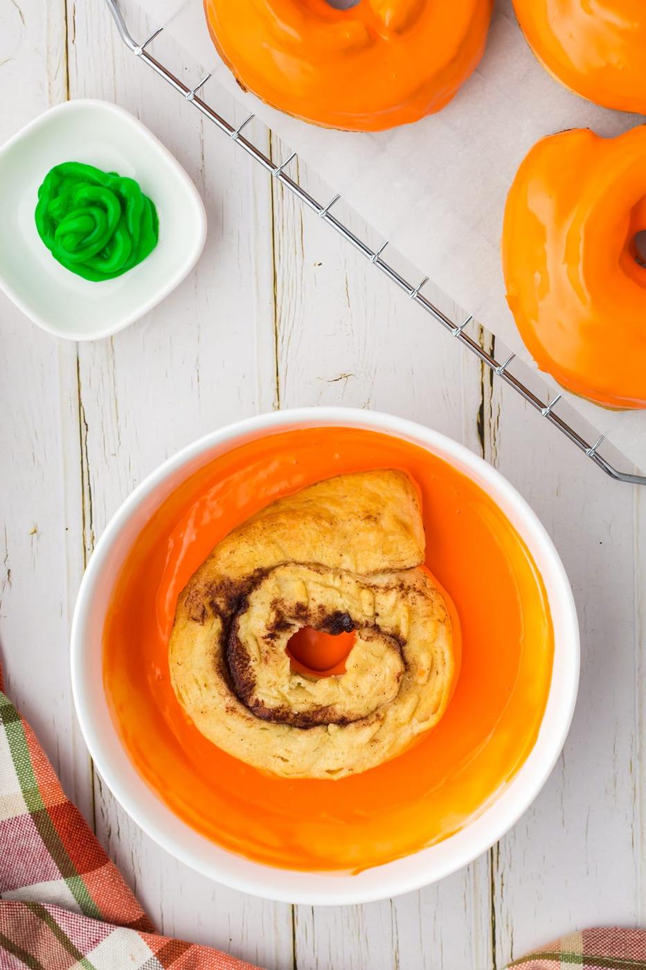 a cinnamon roll donut being dipped into orange icing