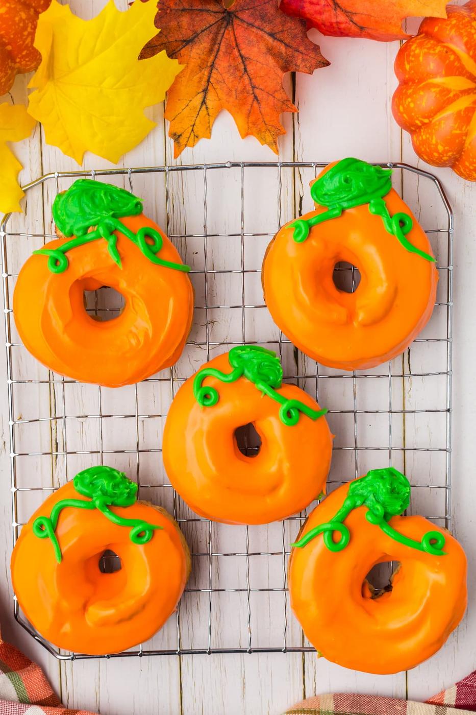 donuts glazed in orange frosting with green leaves and tendrils on top to look like a pumpkin