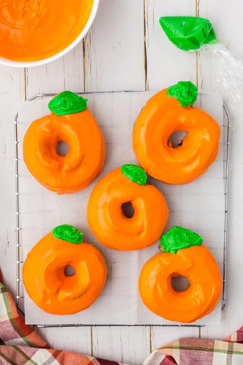 donuts glazed in orange frosting with green leaves and tendrils on top to look like a pumpkin
