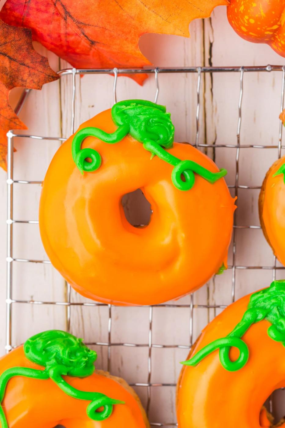 donuts glazed in orange frosting with green leaves and tendrils on top to look like a pumpkin