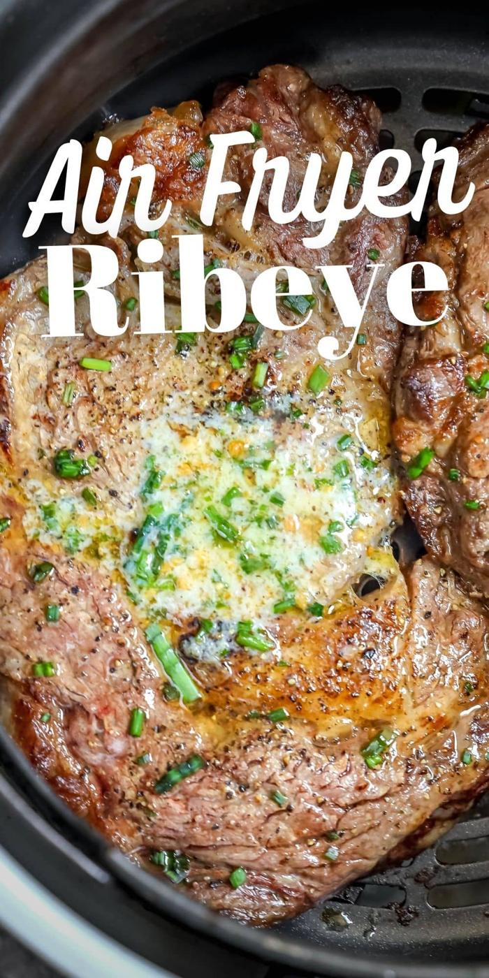 two steaks in an air fryer basket with butter and chives on them