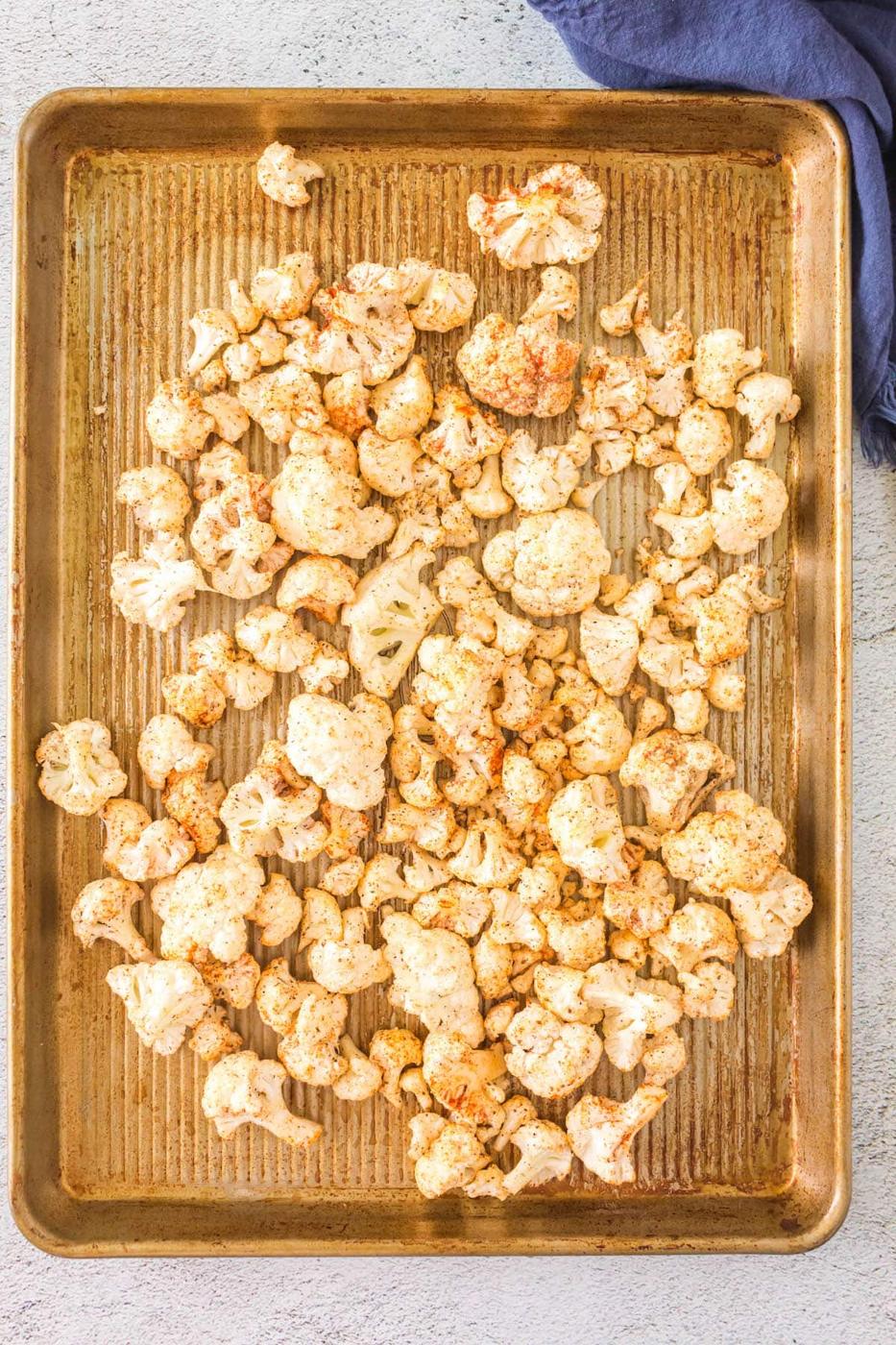 raw cauliflower tossed in spices on a baking sheet