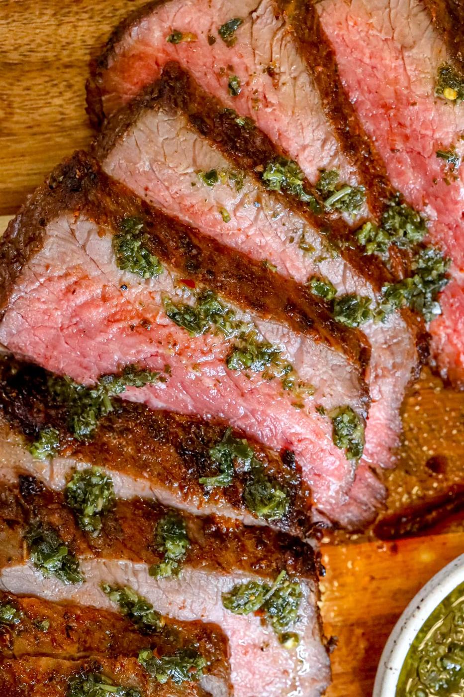 picture of sliced tri tip steak on a cutting board with chimichurri sauce on top