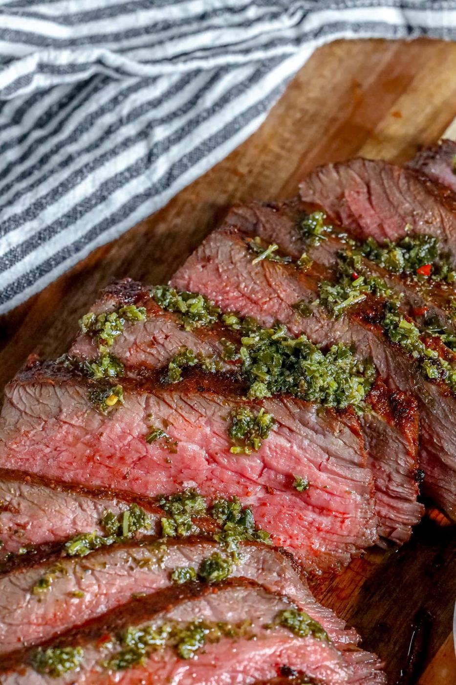 picture of sliced tri tip steak on a cutting board with chimichurri sauce on top