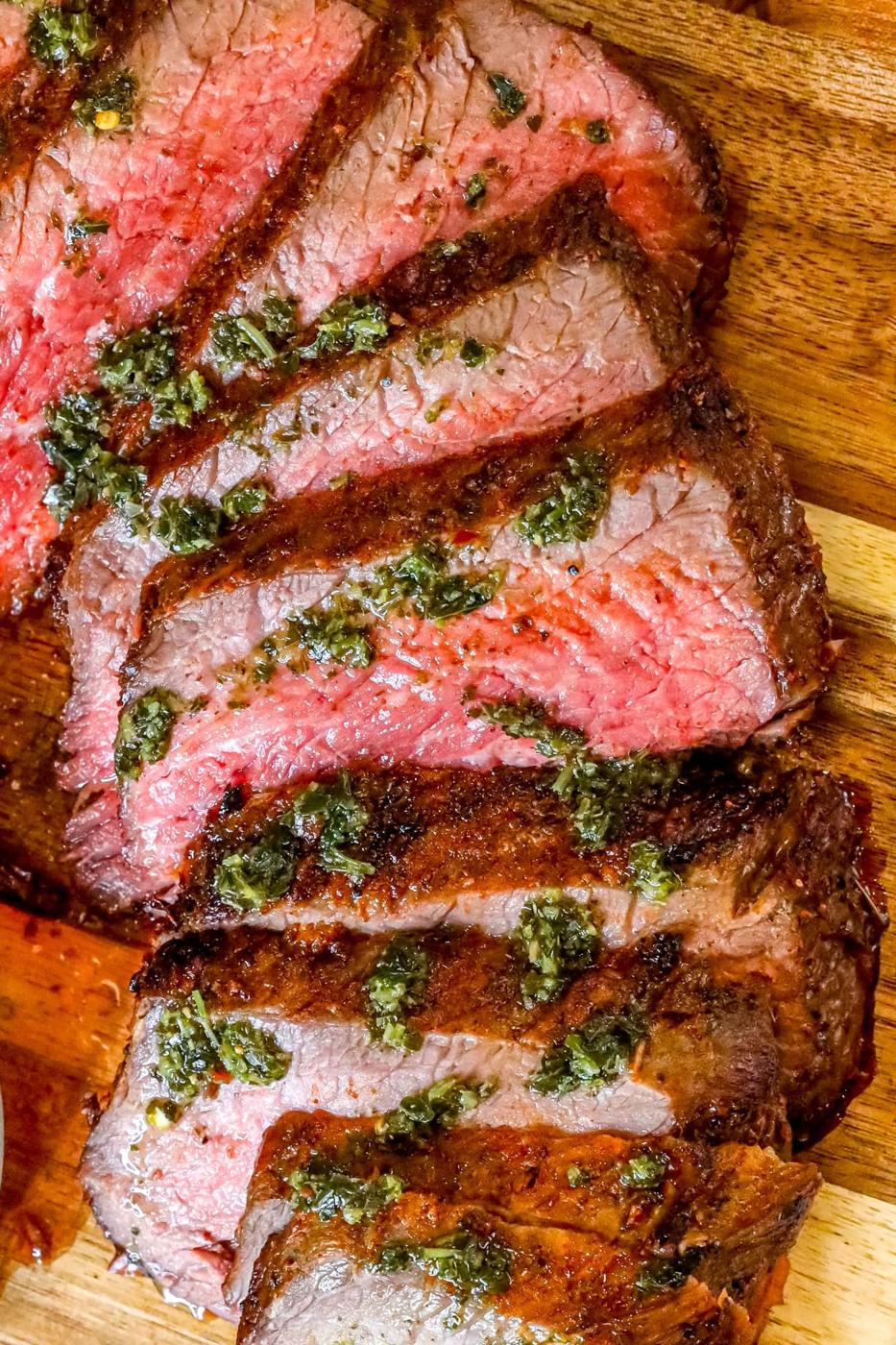 picture of sliced tri tip steak on a cutting board with chimichurri sauce on top