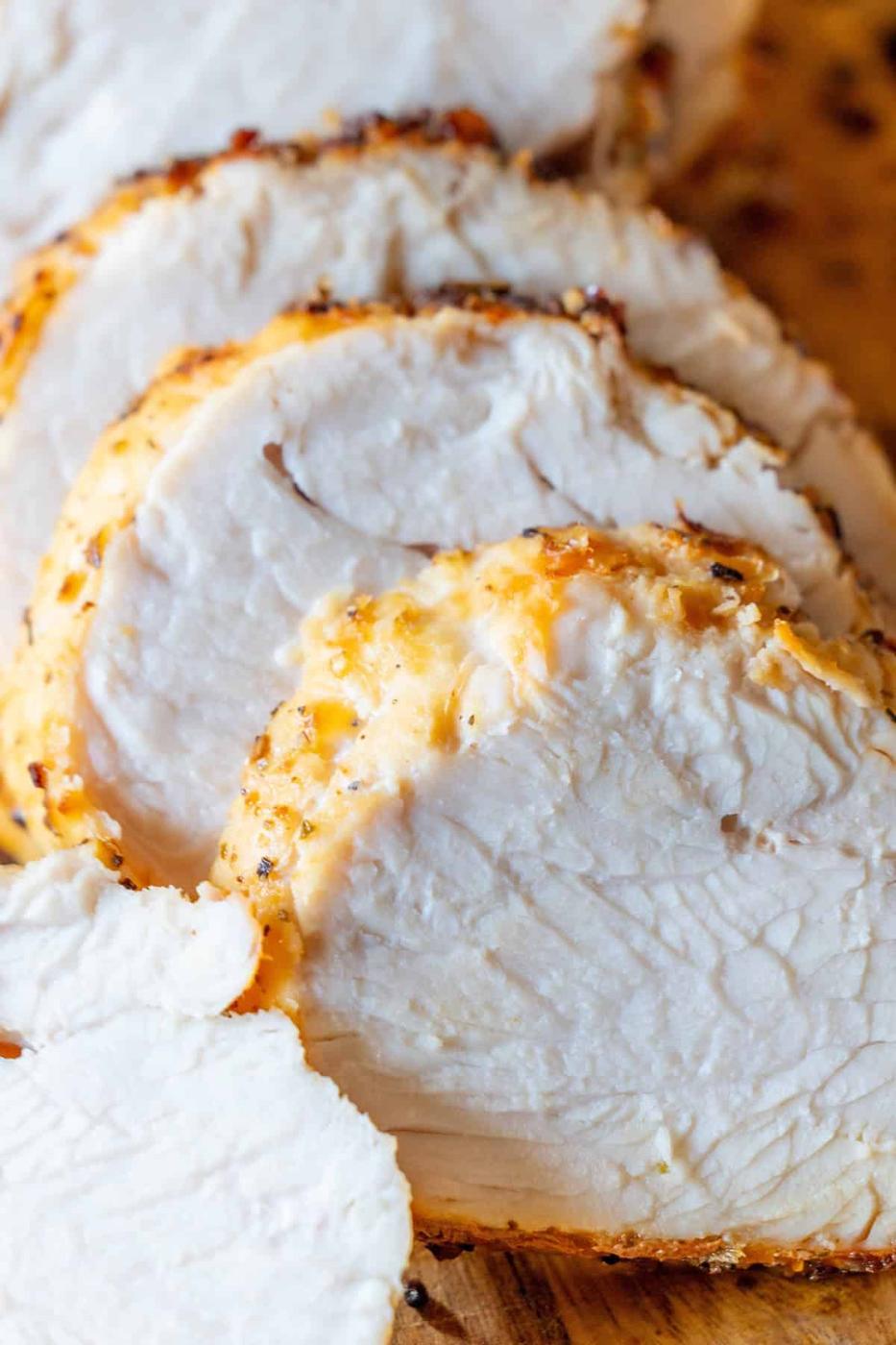 Close-up of several slices of cooked, seasoned turkey breast arranged on a wooden cutting board, freshly prepared in the air fryer.
