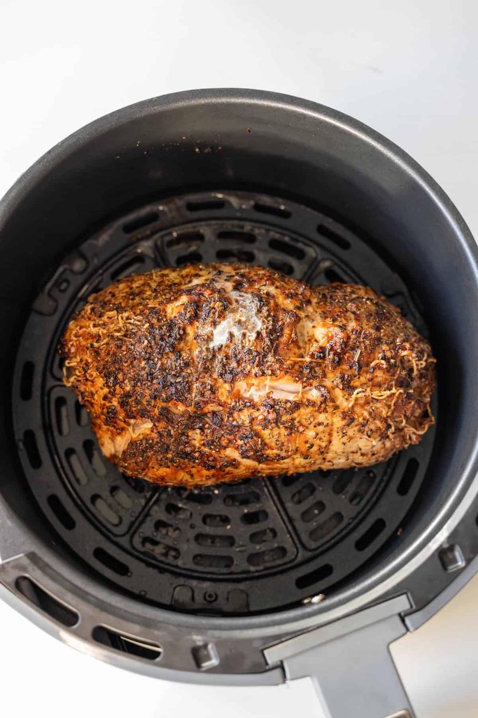 A seasoned Air Fryer Turkey Breast sits inside the basket of an air fryer on a white background.