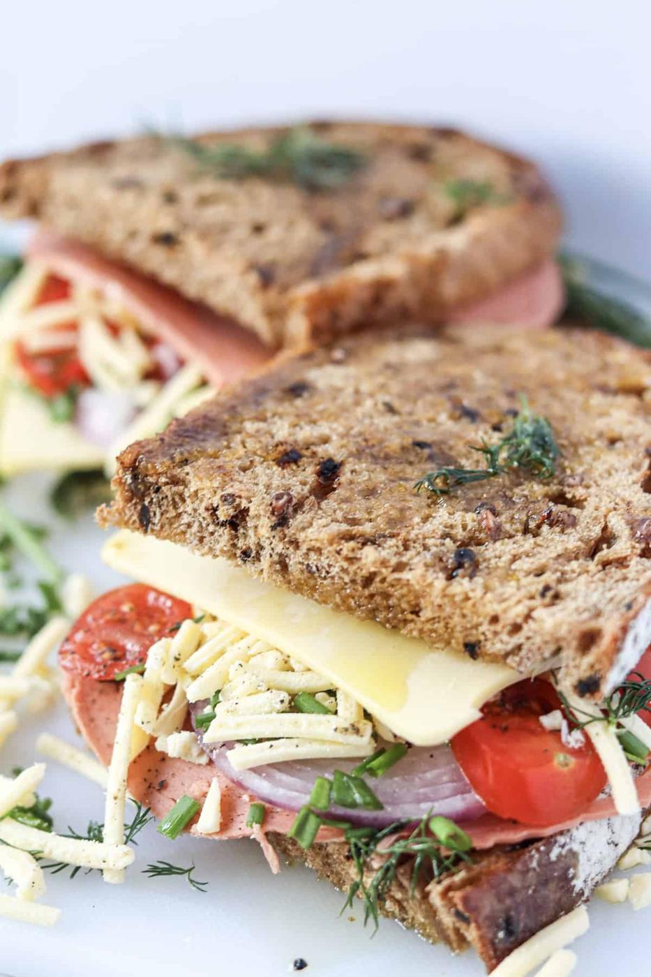 A sandwich with ham, cheese, tomatoes and dill on a white plate.