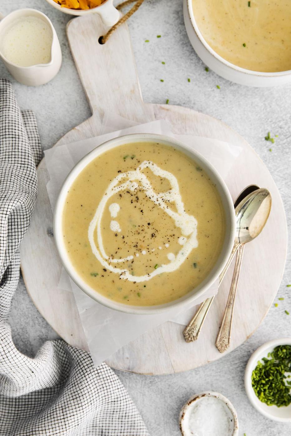 a spoon next to a bowl of cheddar soup with a swirl of cream and crack of pepper on top