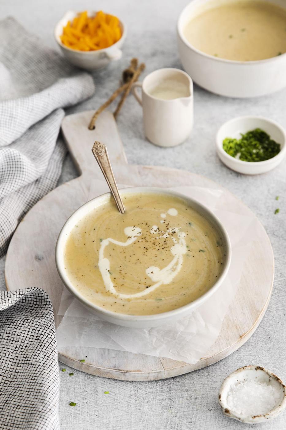 a spoon in a bowl of cheddar soup with a swirl of cream and crack of pepper on top