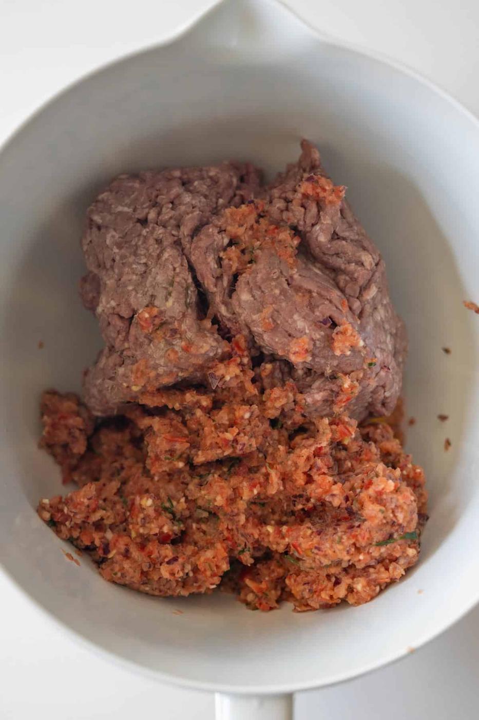 Ground beef and a mixture of finely chopped vegetables or seasonings come together in a white mixing bowl, perfect for preparing flavorful Armenian spiced meat kebabs.