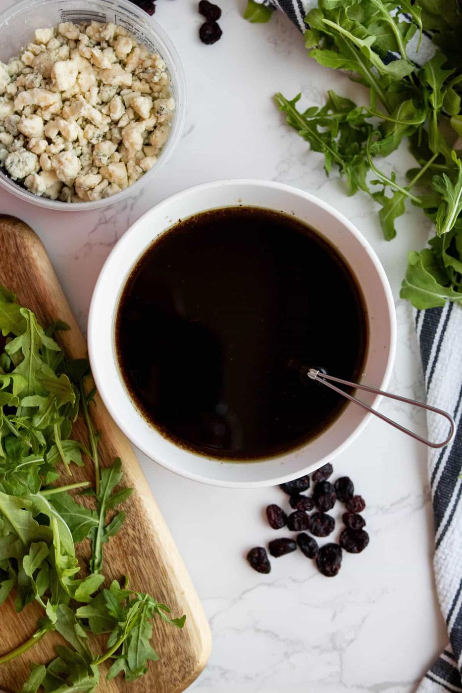 A bowl of arugula, cranberries and blue cheese dressing with walnuts.
