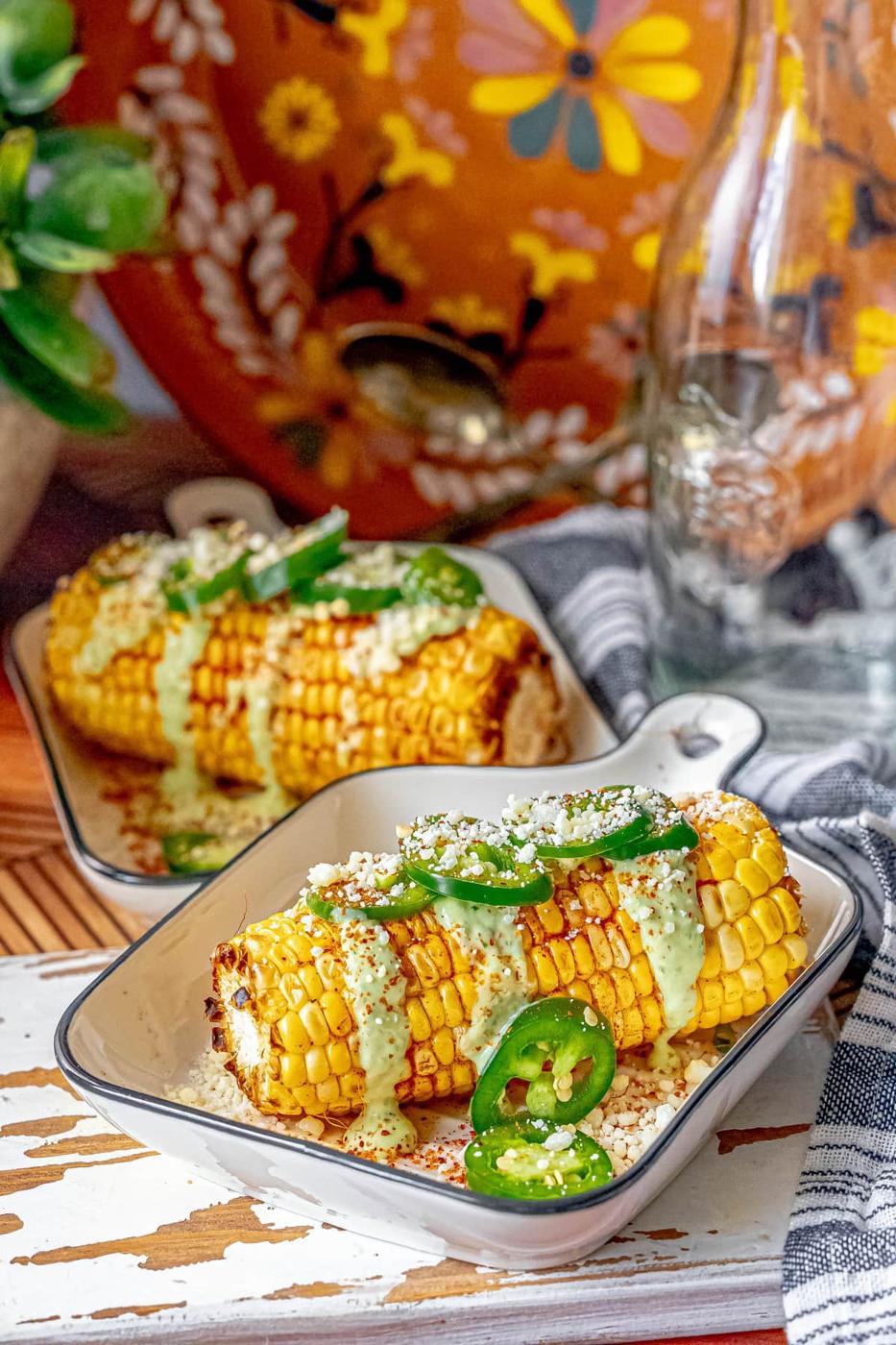 picture of elotes corn cob with crema, cheese, jalapenos, and spices on top