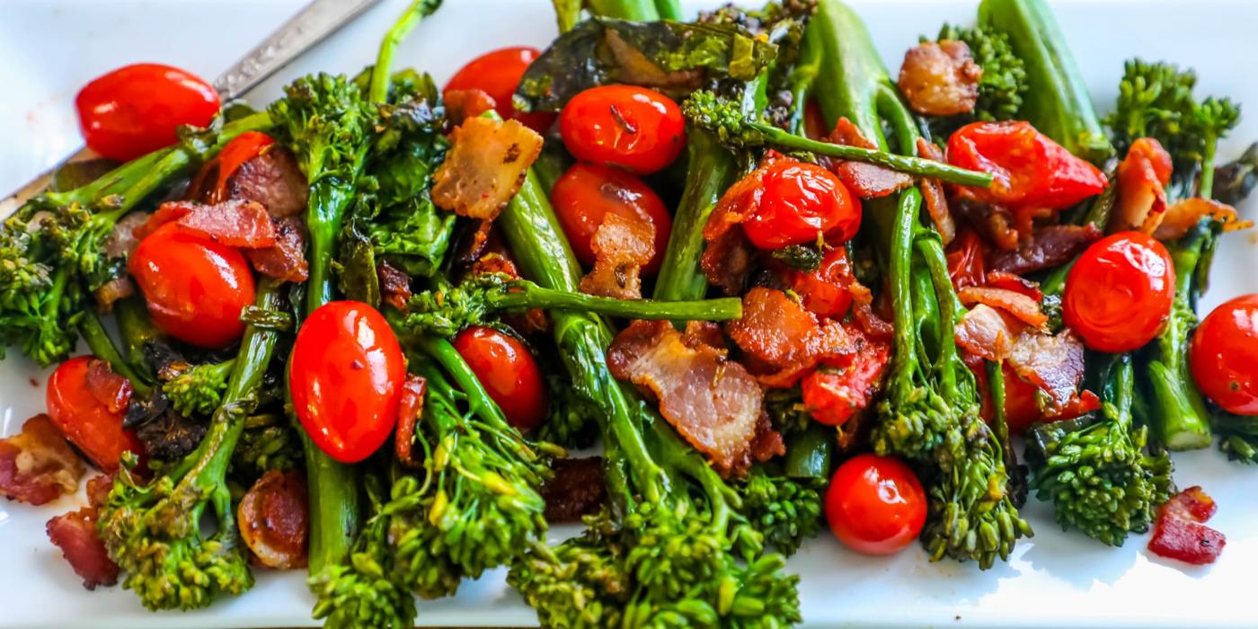 picture of a white plate with broccolini, bacon, and cherry tomatoes on it.