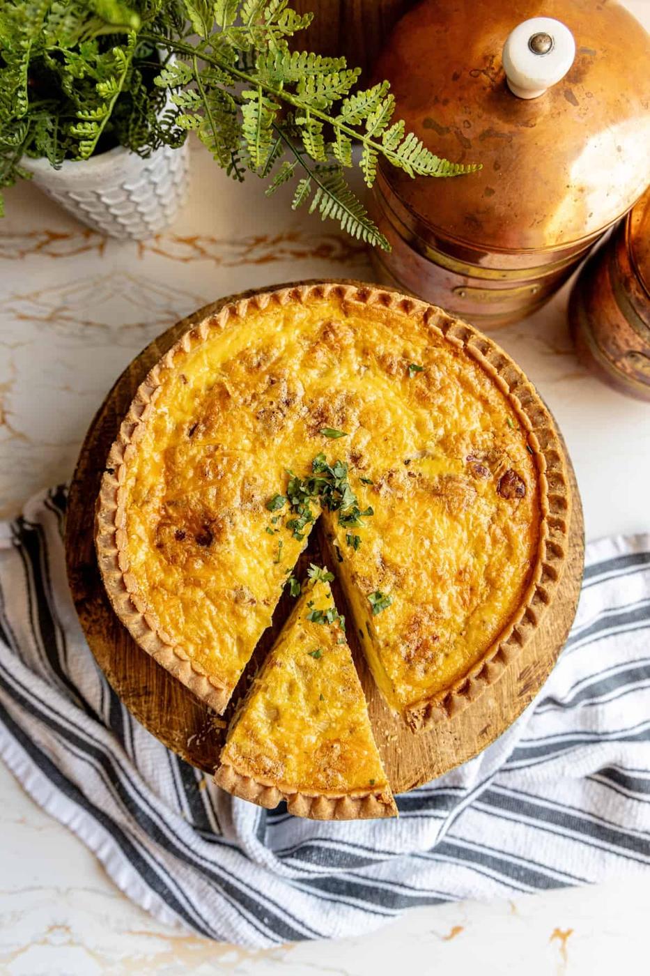 A bacon and cheese quiche with a slice missing.