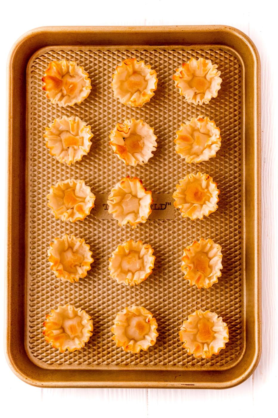 A baking sheet full of mini raspberry tarts on a white background.