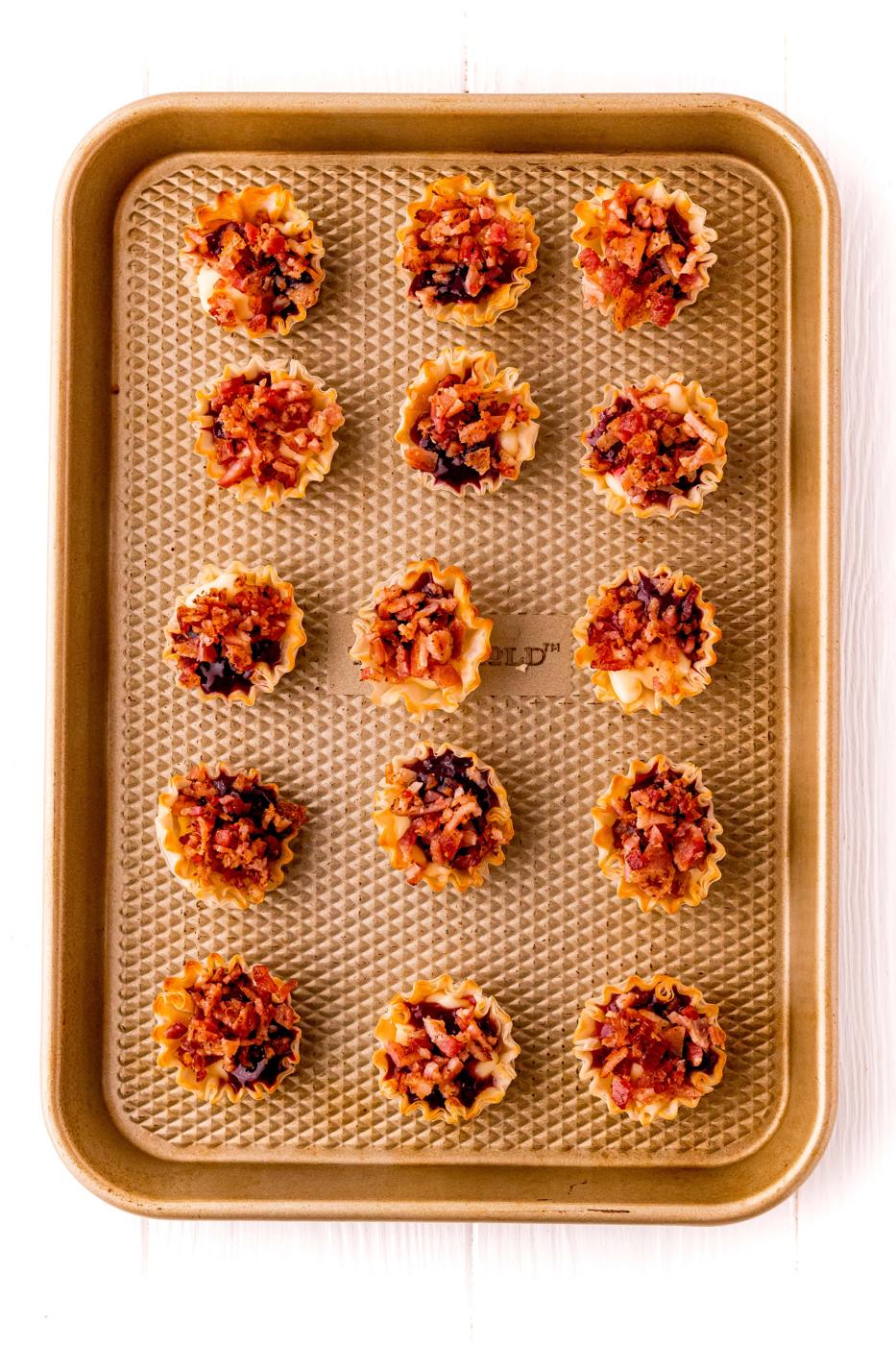 A baking sheet filled with small bites of bacon and a raspberry cheese recipe.