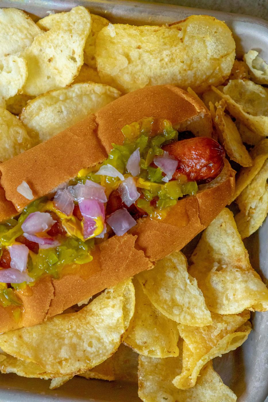picture of bacon-wrapped hot dog in a bun topped with mustard, relish, and onions