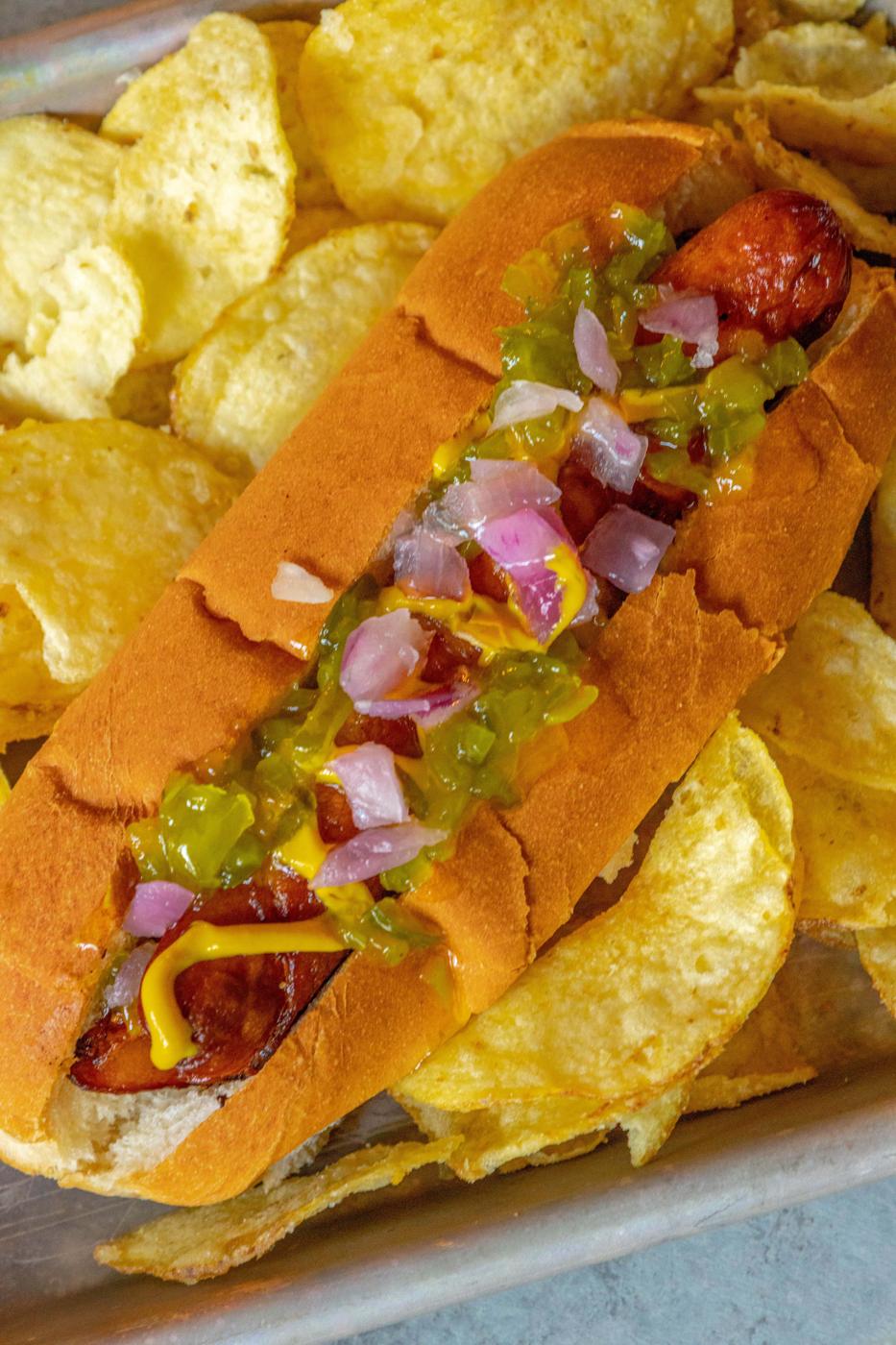 picture of bacon-wrapped hot dog in a bun topped with mustard, relish, and onions