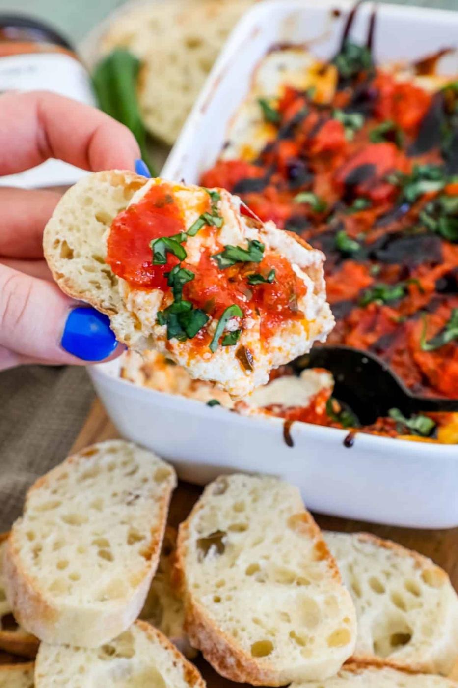 A person dipping bread into a dish of bruschetta dip.