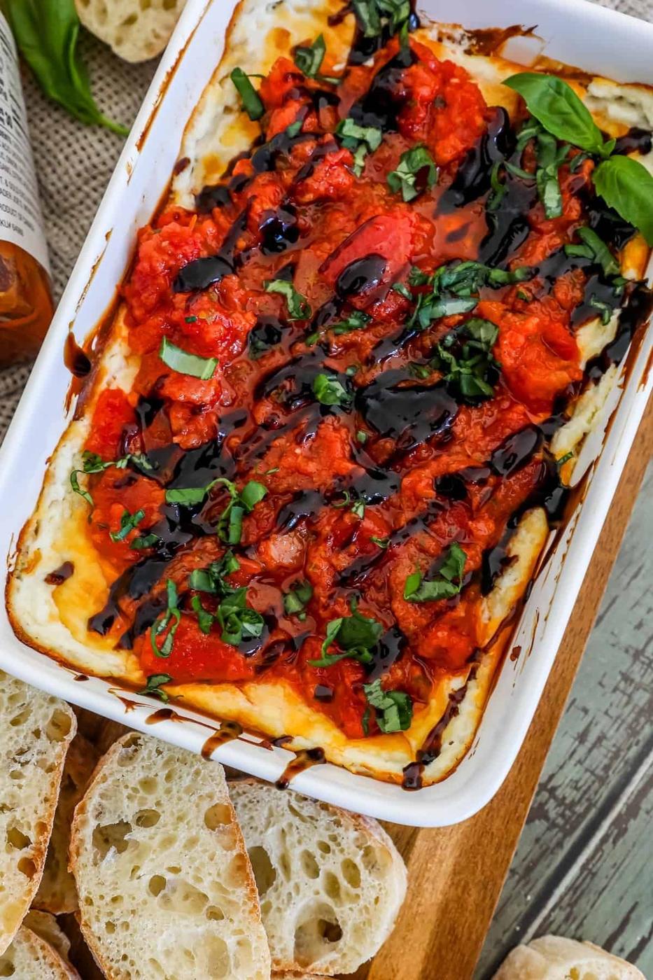 A dish of tomato and basil dip, served on a cutting board.