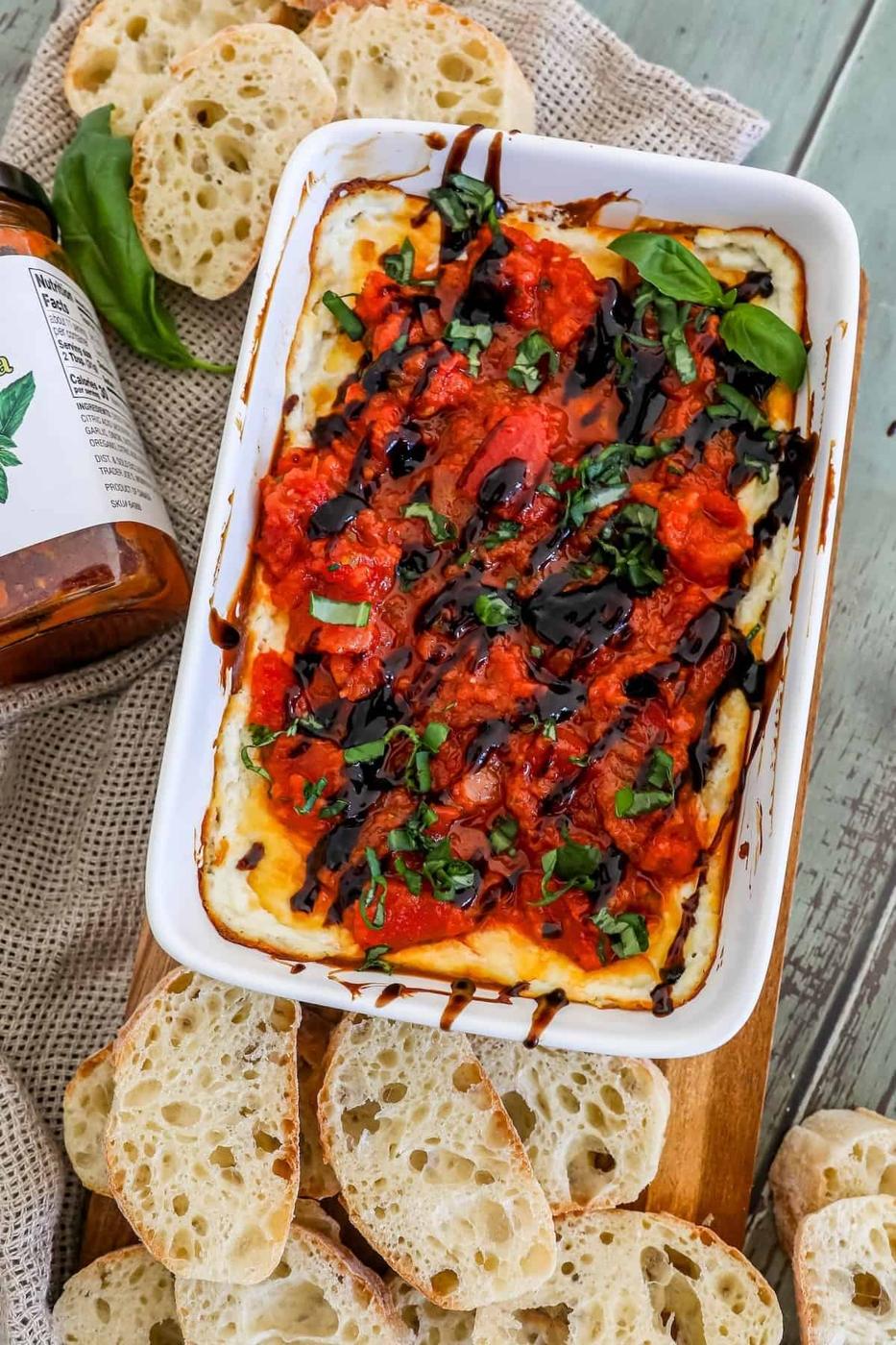 A dish of bruschetta dip with bread on a cutting board.