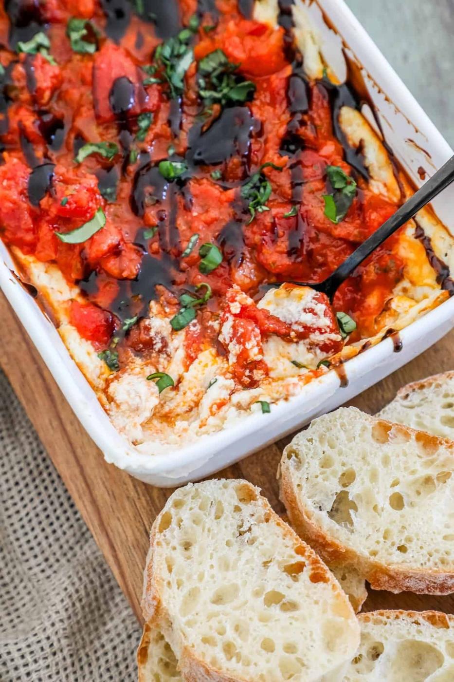 A dish of tomato dip with bread on a cutting board, served with baked goat cheese and bruschetta dip.