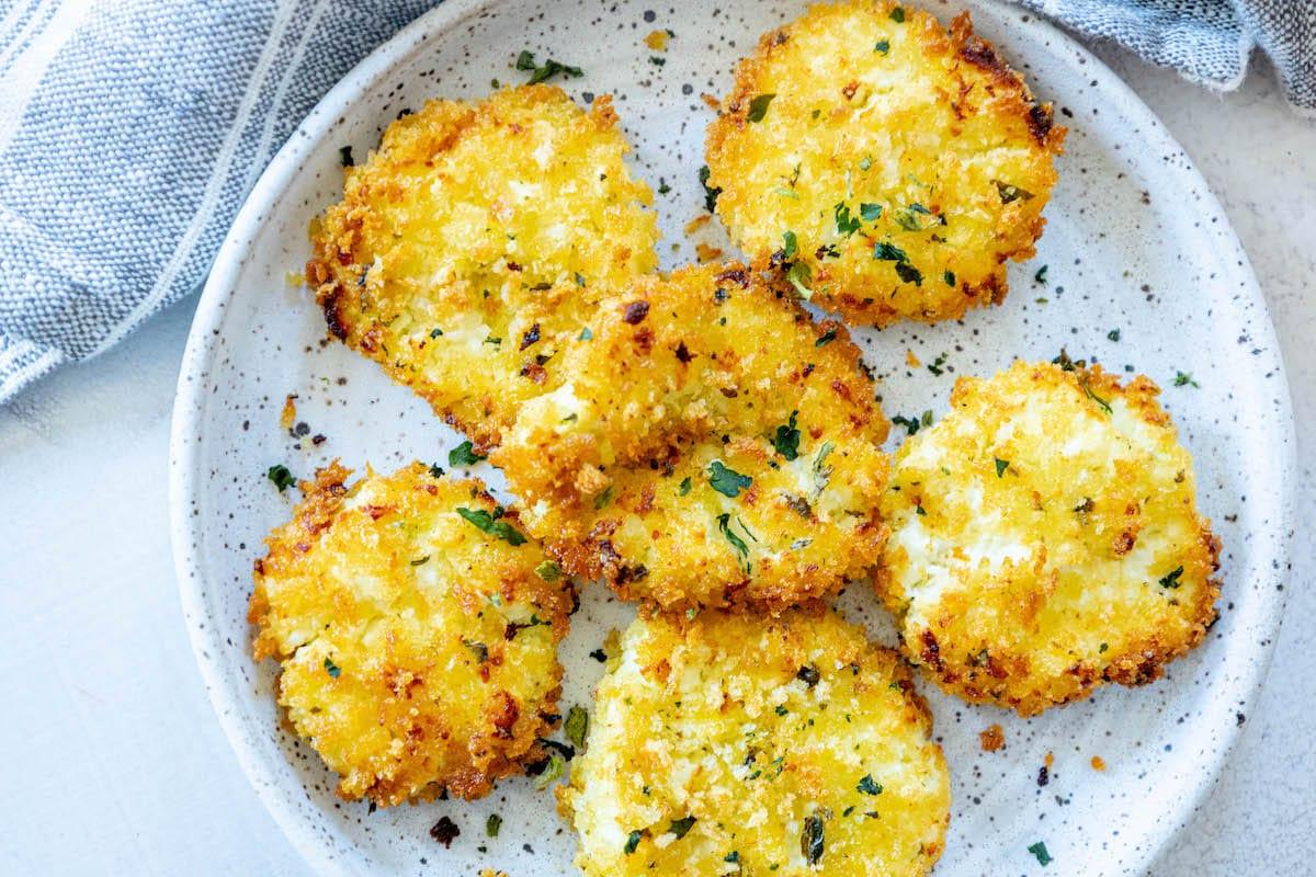 golden baked breaded goat cheese balls topped with herbs on a white speckled plate