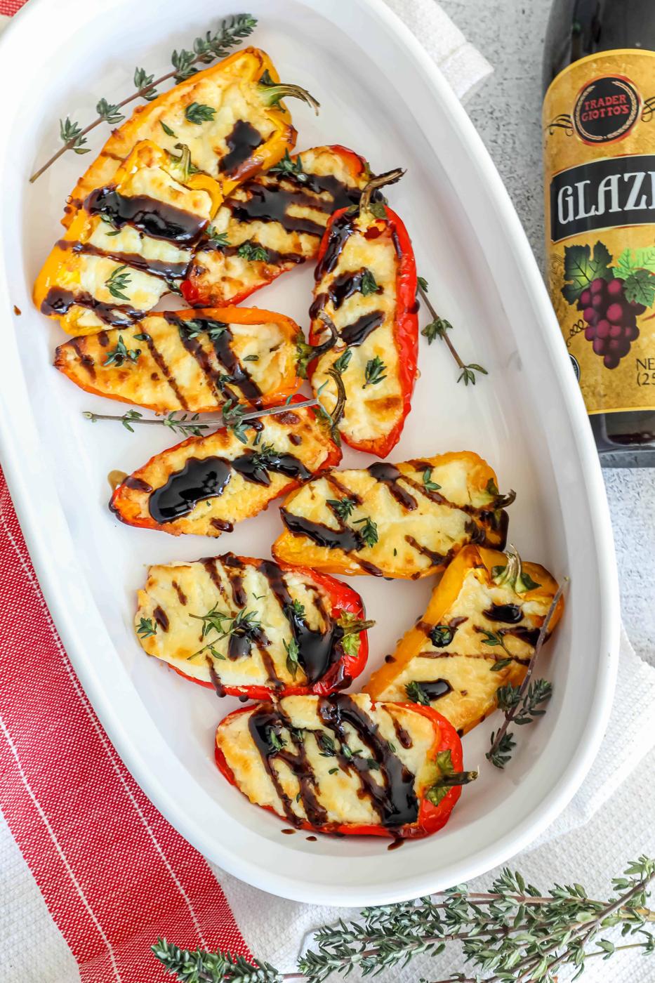 Grilled peppers with balsamic glaze on a white plate next to a bottle of wine.