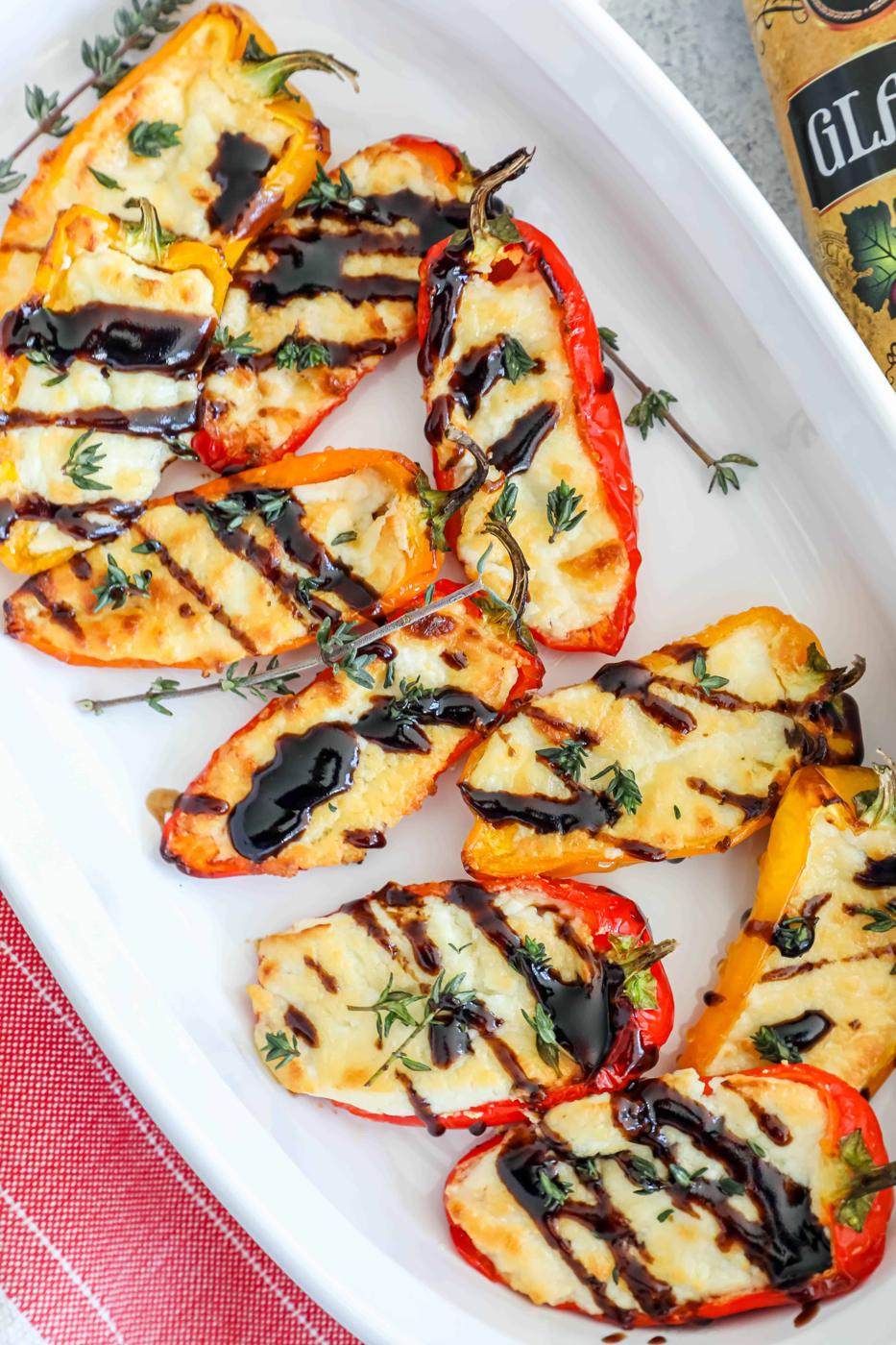 Grilled peppers on a white plate with a side of baked goat cheese and a bottle of olive oil.