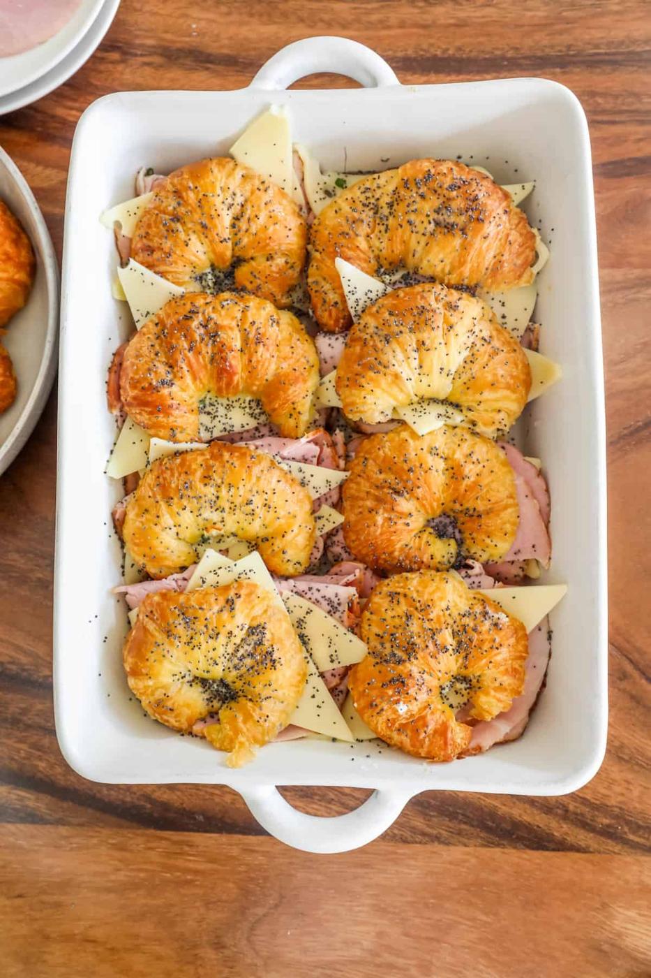 Ham and cheese croissants in a white dish on a table.