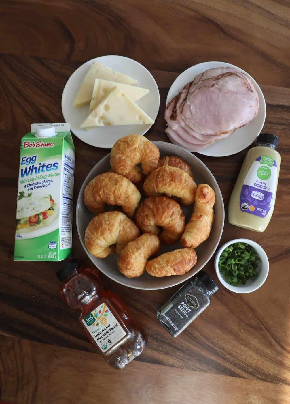 A plate of croissants, ham, cheese, and a bottle of milk on a table.