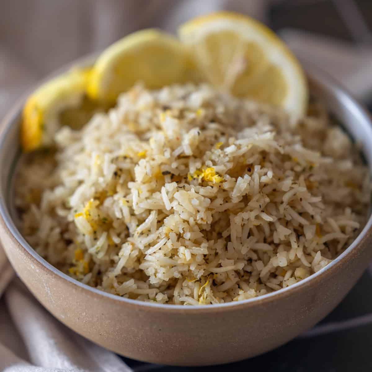 A bowl of Baked Lemon Rice garnished with lemon zest, served with three lemon slices on the rim.
