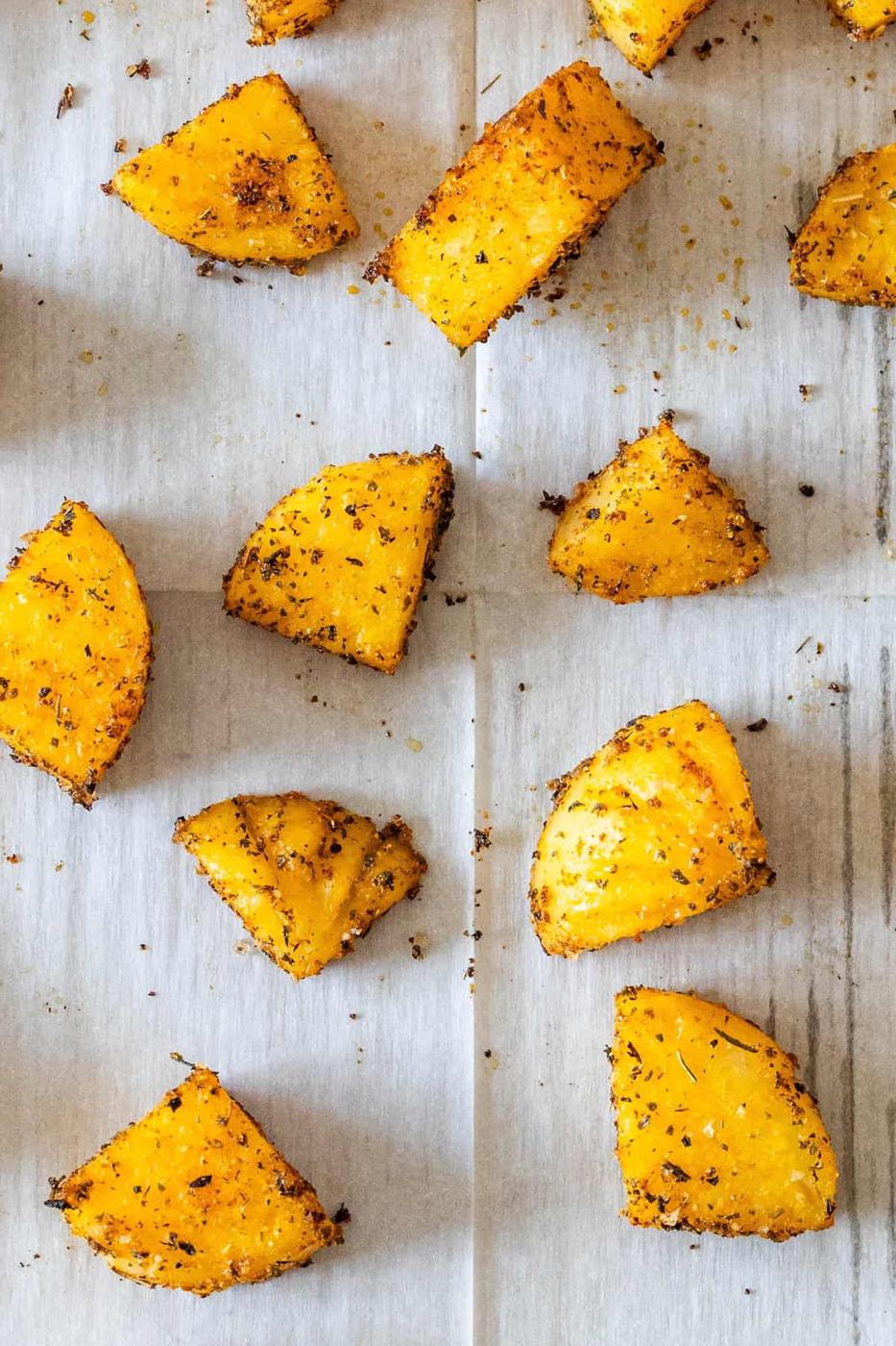 Roasted golden beet wedges coated with herbs and spices make a vibrant baked appetizer, beautifully arranged on a sheet of parchment paper.