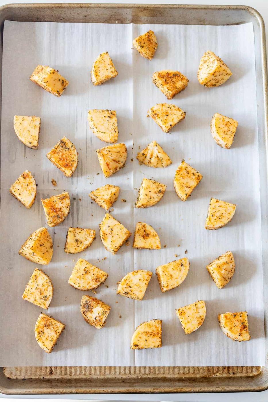 Seasoned potato wedges are arranged on a parchment-lined baking sheet, ready for roasting alongside delicious Baked Polenta Bites.