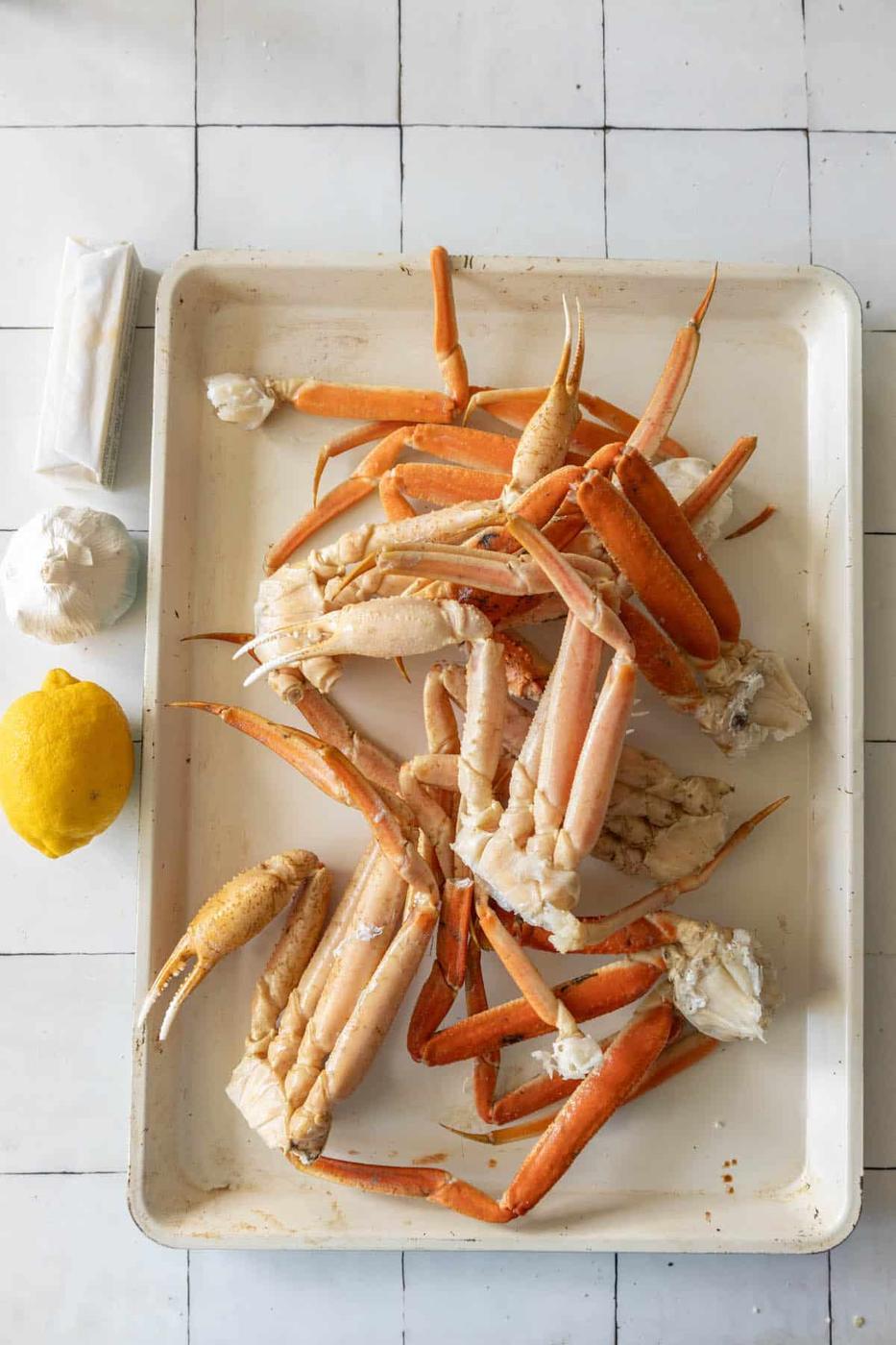 Baked snow crab legs on a white tray with lemon wedges.