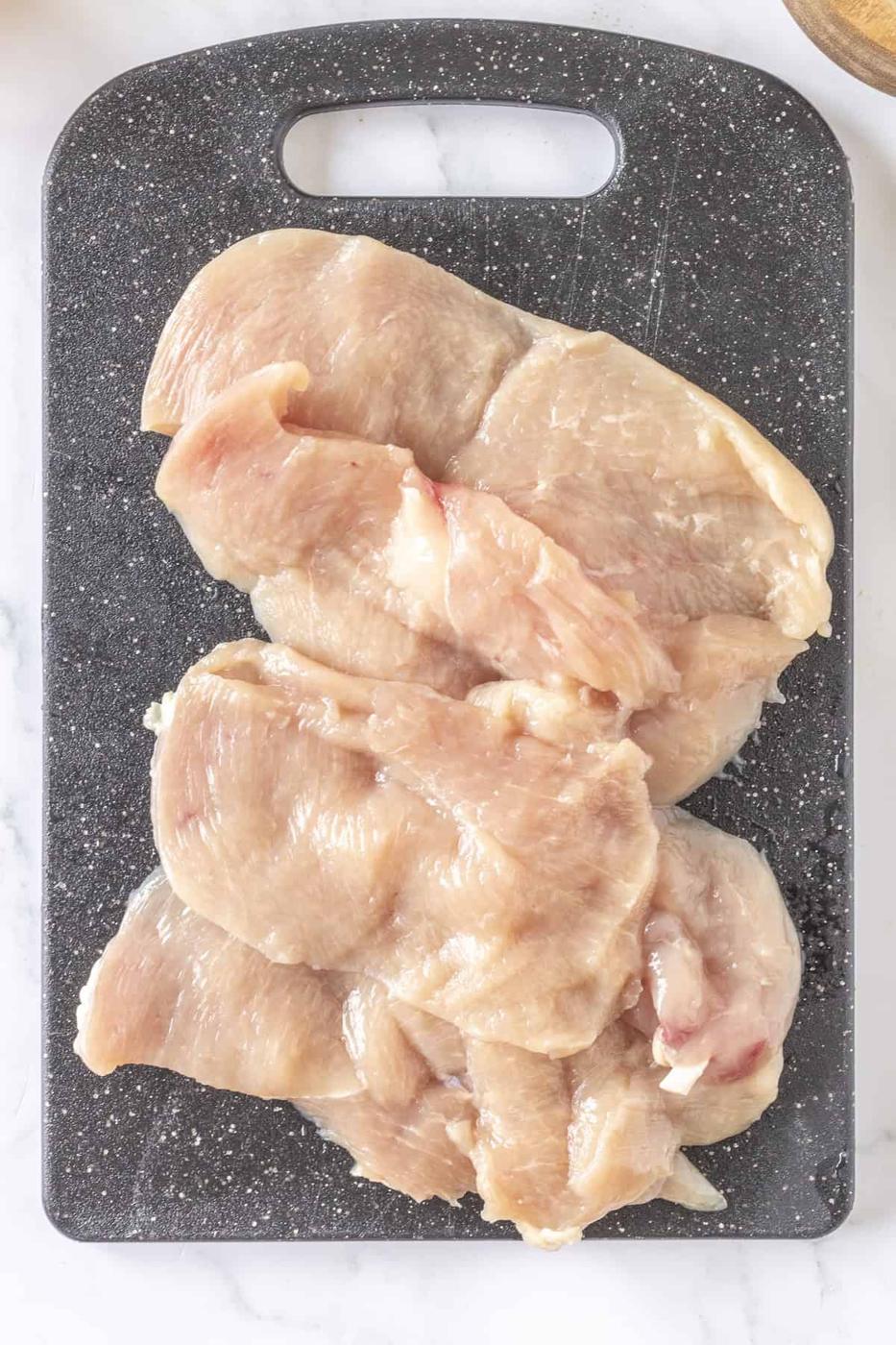 Thin baked chicken breasts rest on a sleek black cutting board, ready to be seasoned and savored.
