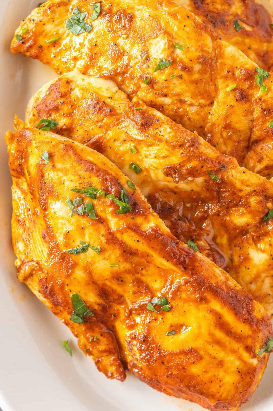 Close-up of seasoned, grilled chicken breasts garnished with fresh herbs on a white plate, showcasing an exquisite chicken breasts recipe.