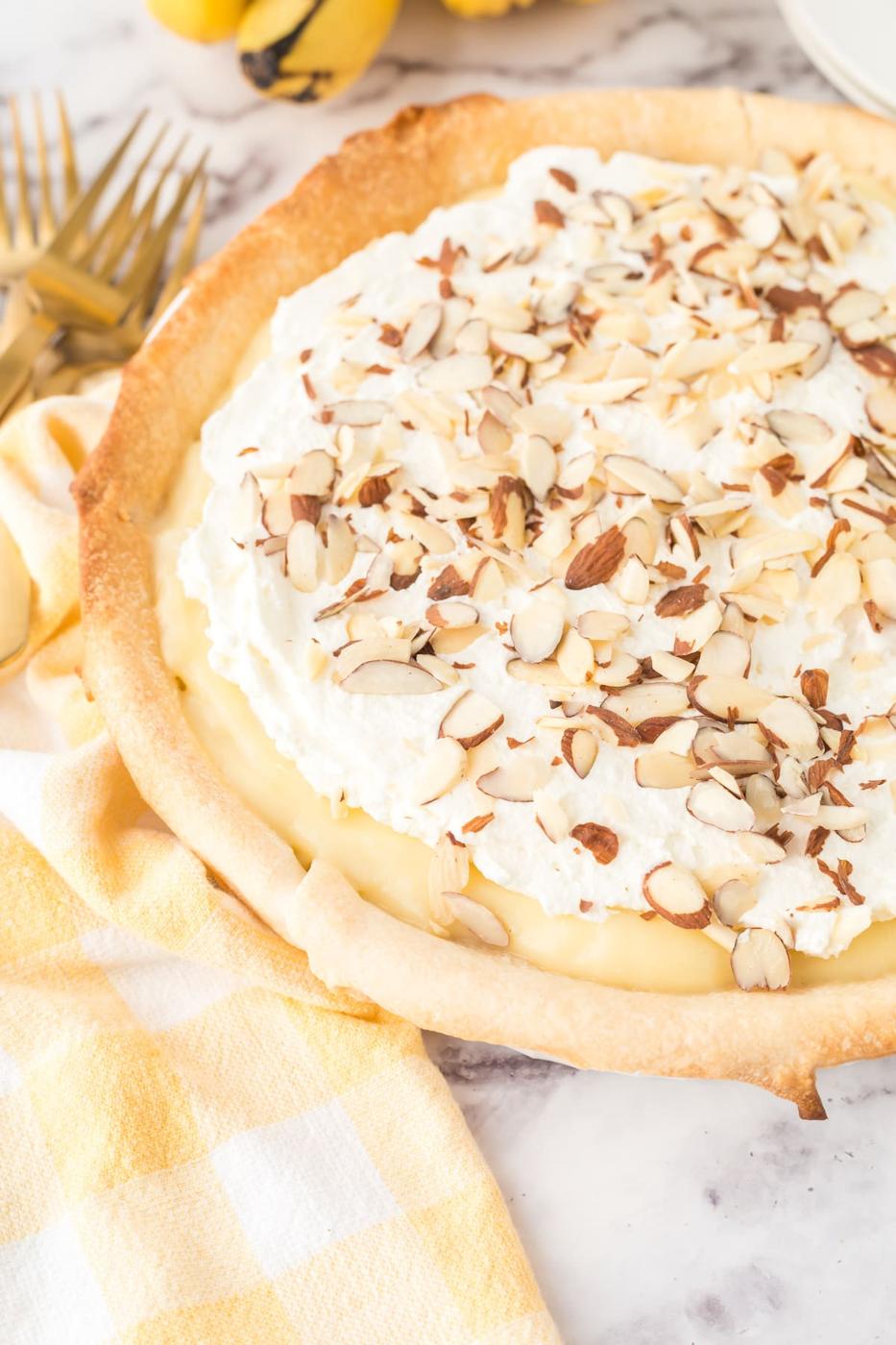 custard banana pie with whipped topping and sliced almonds in a pie pan