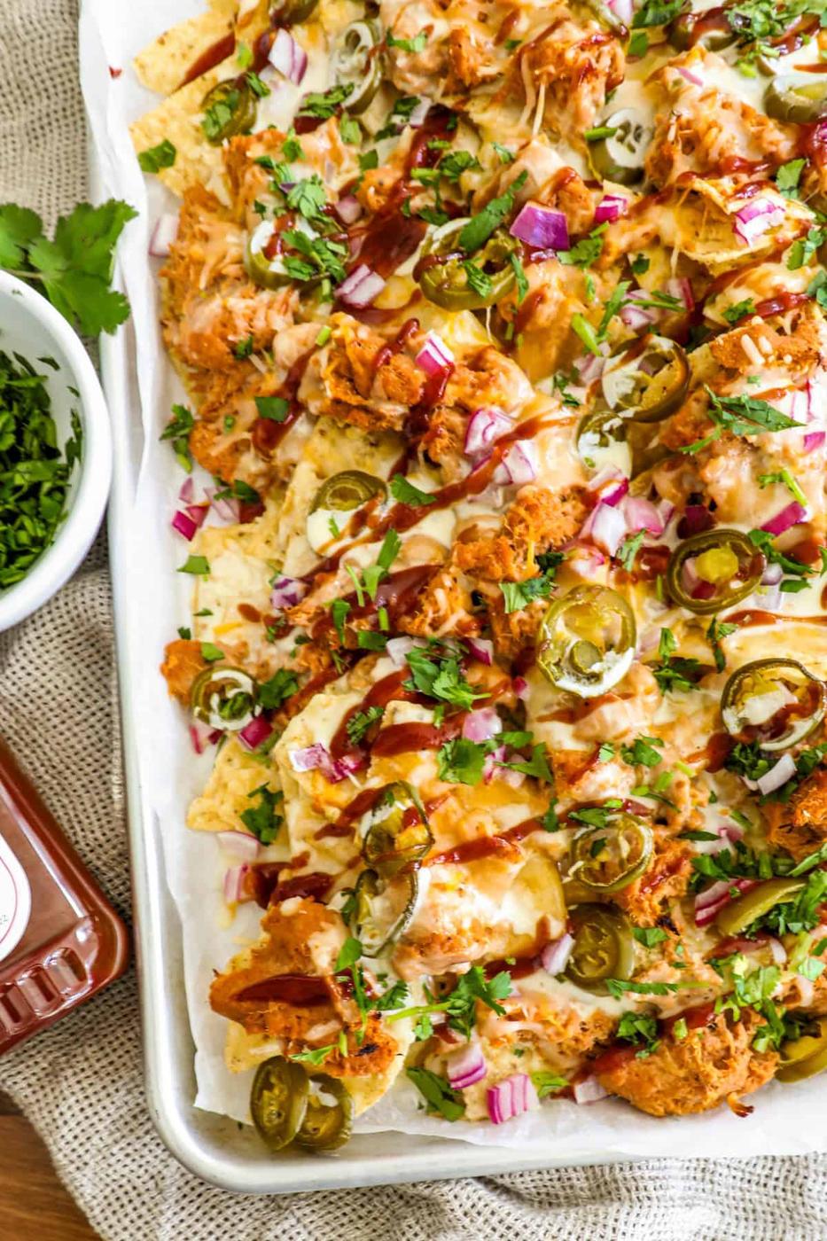 A tray of loaded nachos topped with shredded chicken, jalapeños, red onions, melted cheese, and garnished with fresh cilantro.