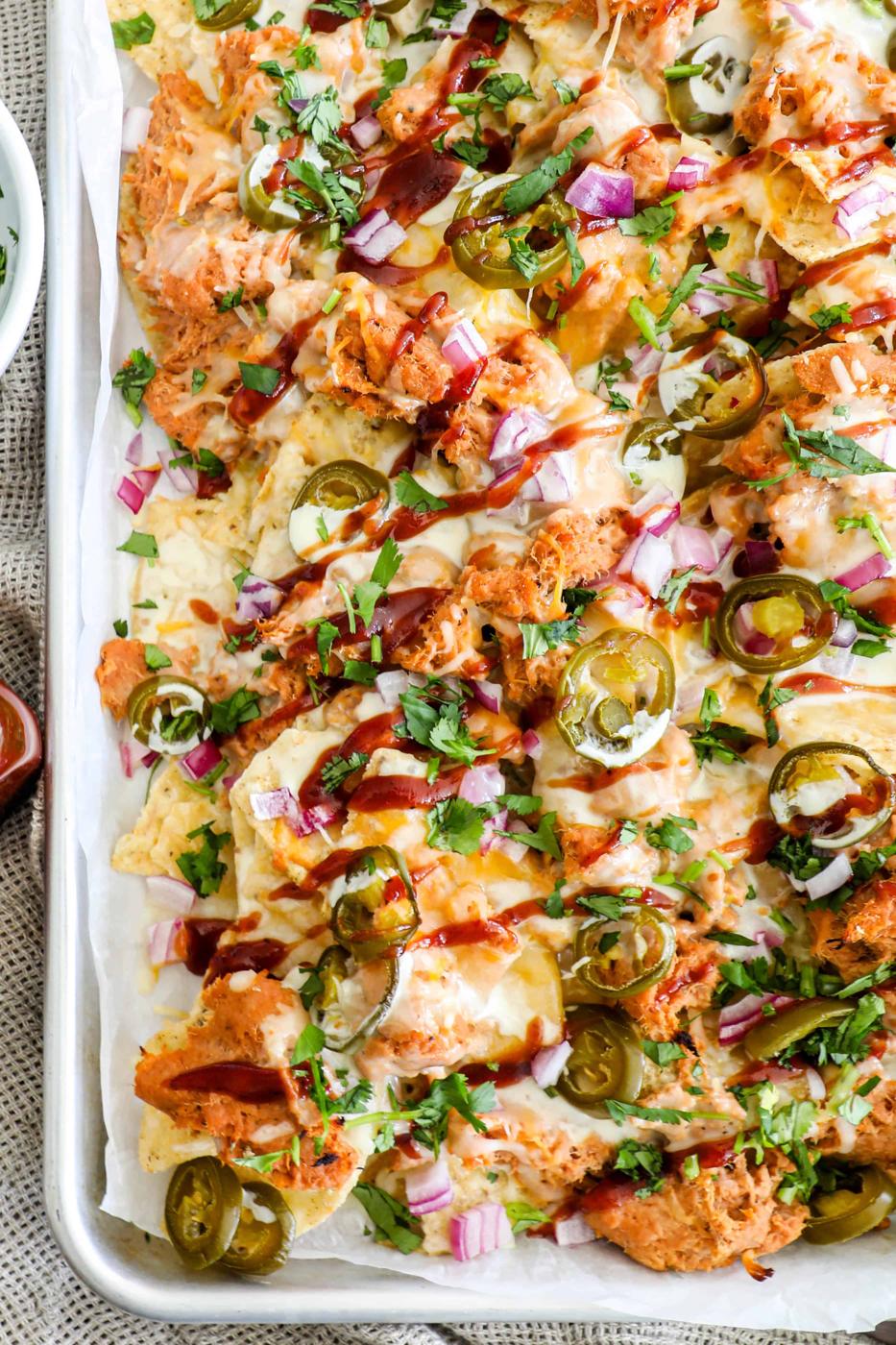 A tray of nachos topped with melted cheese, shredded chicken, jalapeños, red onions, and fresh cilantro.