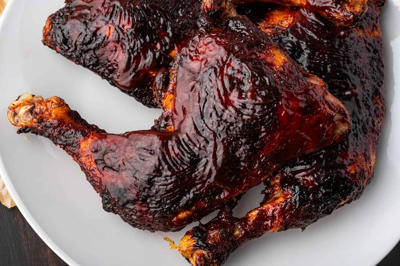 A close-up of succulent chicken legs with a dark, glossy BBQ glaze sits enticingly on a gray plate.