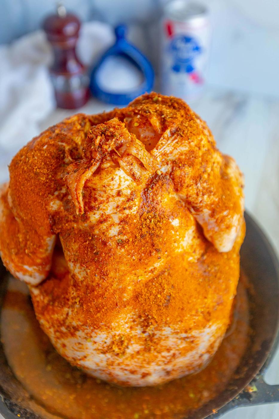 seasoned raw whole chicken with a beer can in the cavity on a cast iron pan