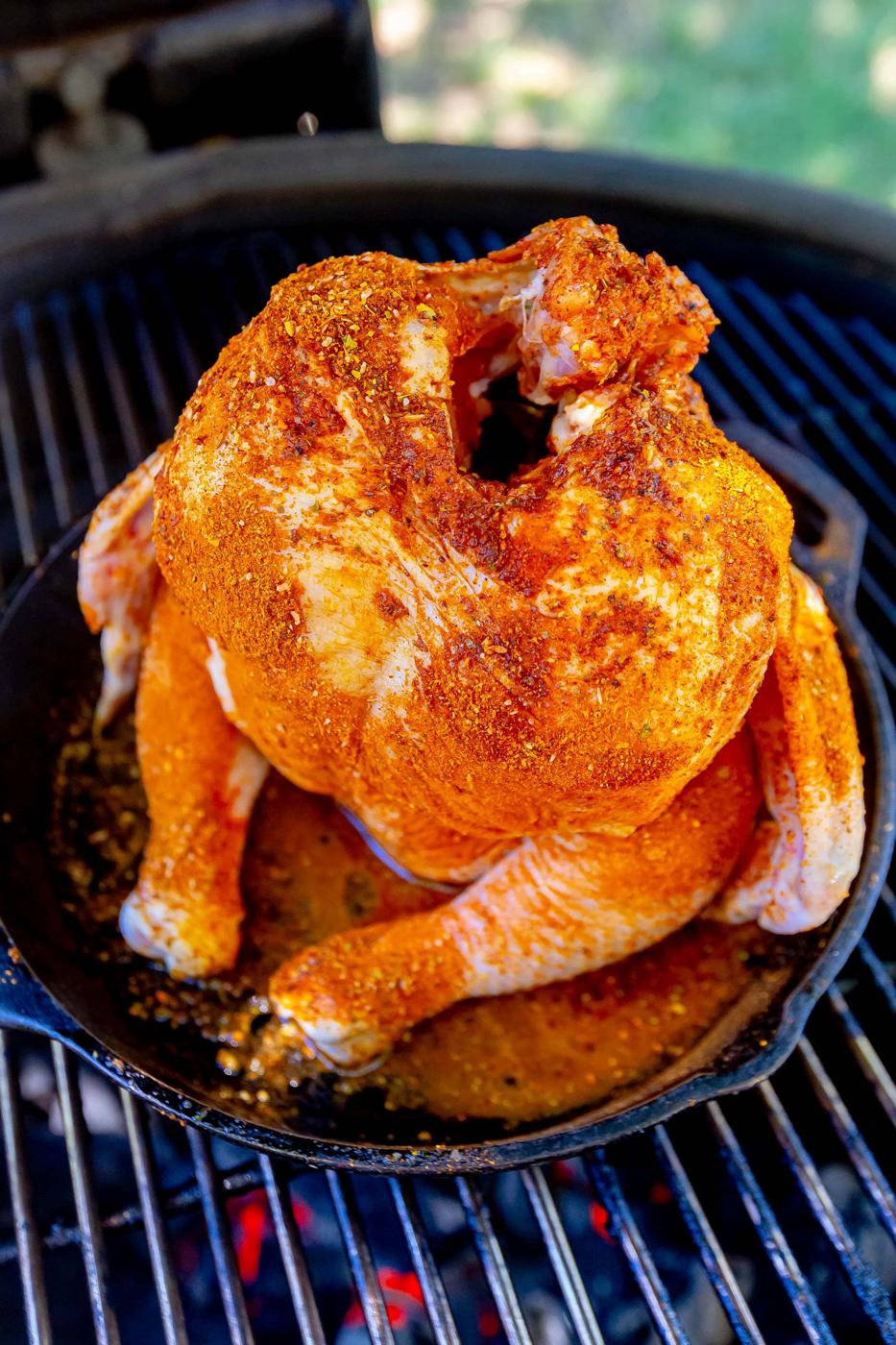 raw seasoned beer can chicken in a cast iron pan on a grill