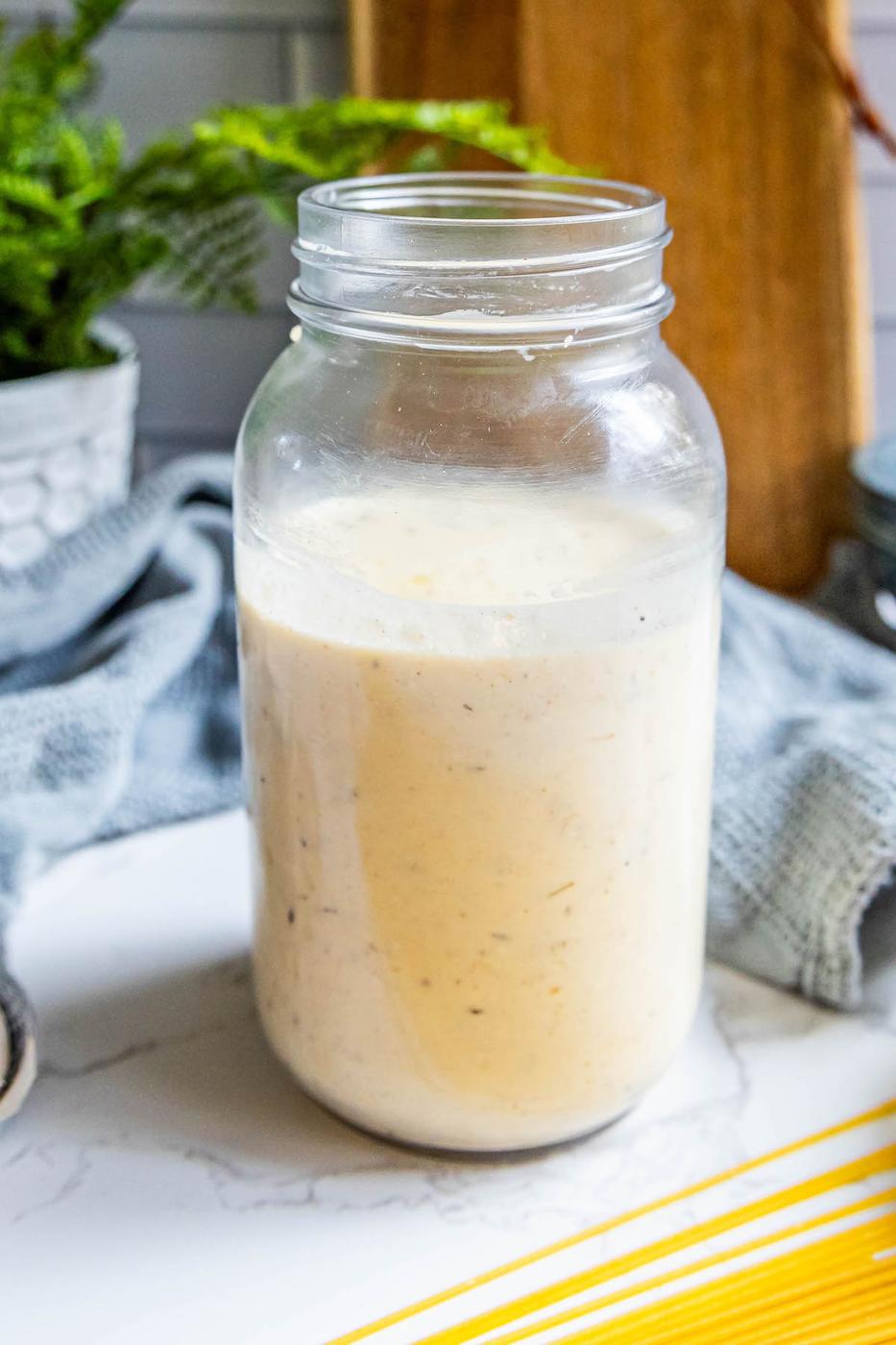 A mason jar filled with the best alfredo sauce sitting on a counter.