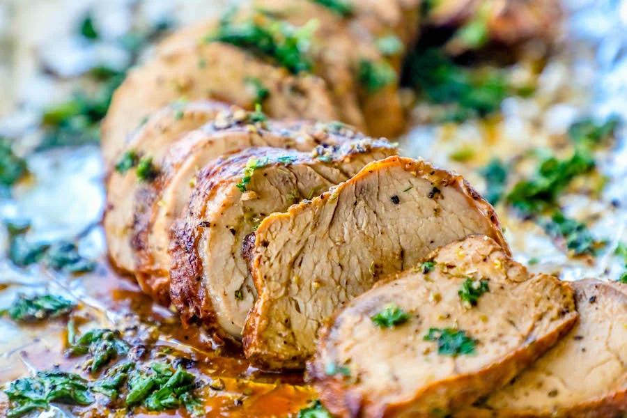 Picture of pork tenderloin sliced and garnished with parsley on tinfoil.