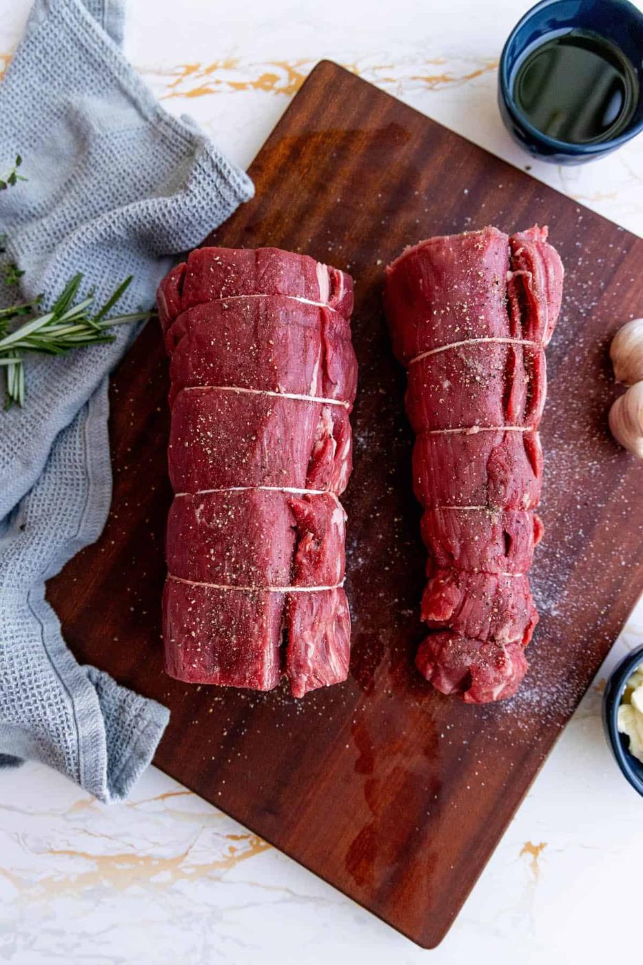 Two pieces of garlic herb beef tenderloin on a wooden cutting board.