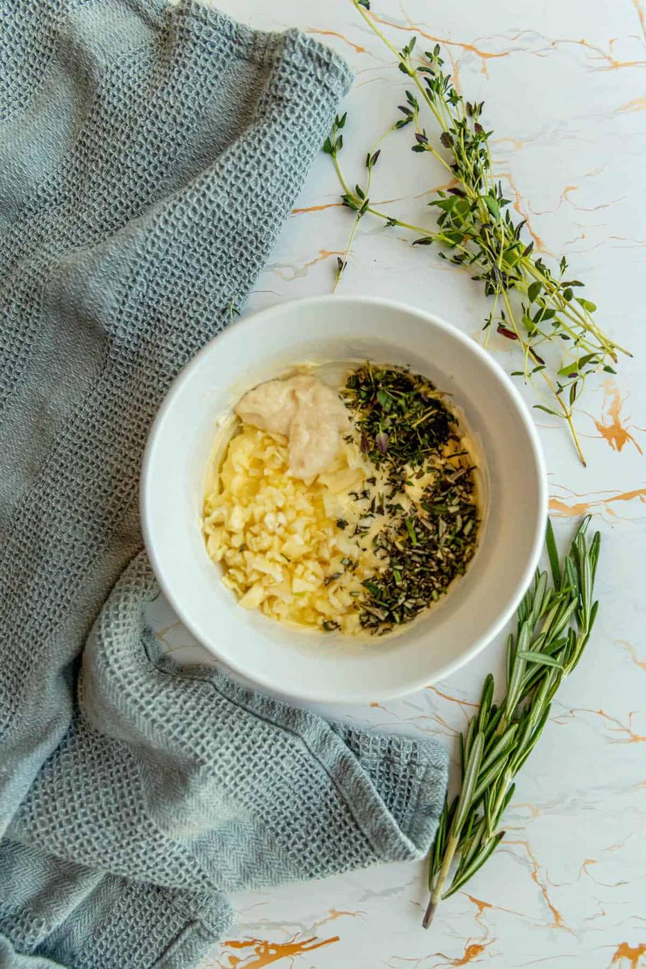 A bowl of hummus with sprigs of thyme and garlic.
