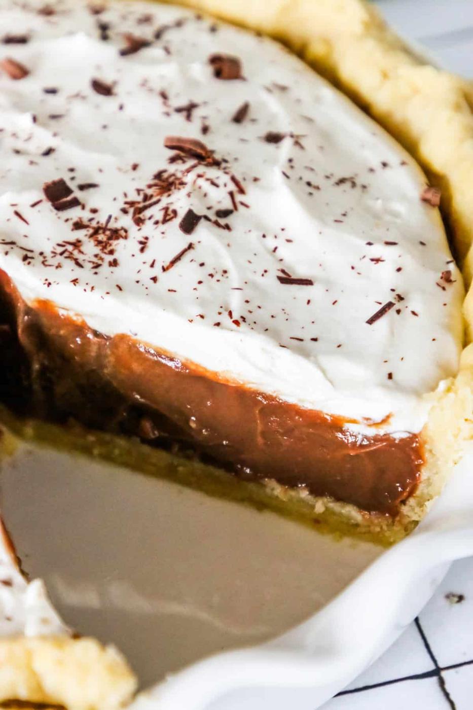 Close-up of a chocolate pie topped with whipped cream and chocolate shavings, with a slice partially taken out.